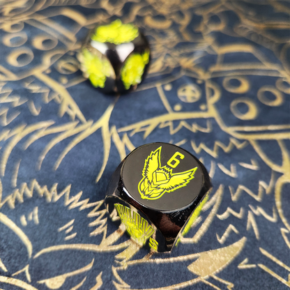 Two black metal dice with yellow graphics, resting on a dark blue patterned fabric surface.