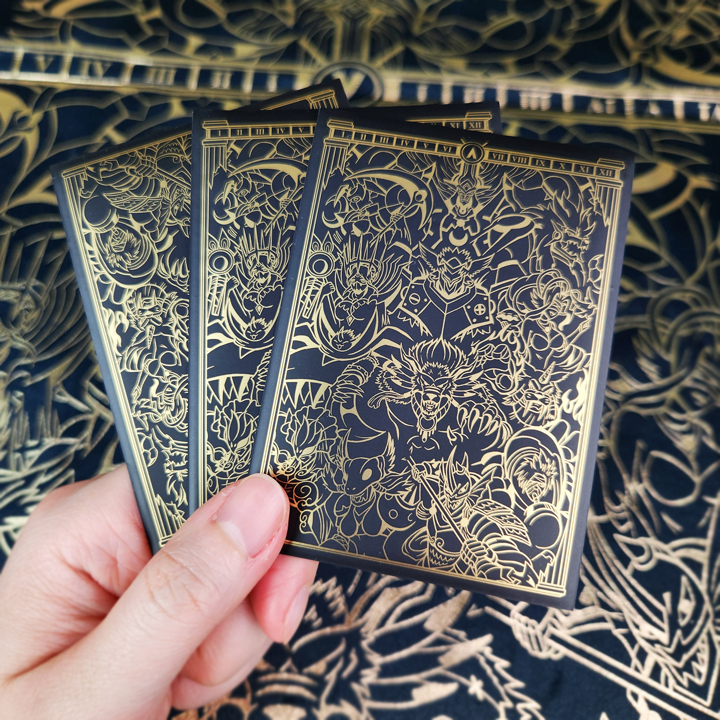 Three illustrated playing cards with dark backs featuring intricate gold line art, set against a matching patterned navy and gold surface.