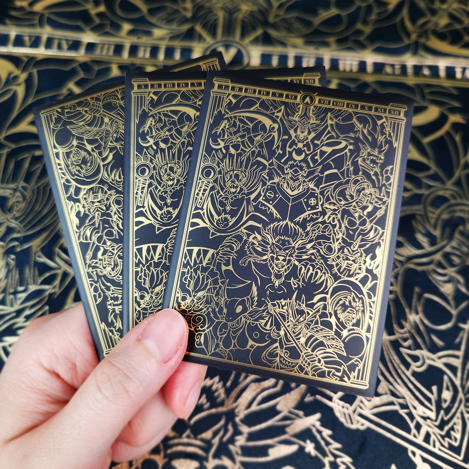 Three illustrated playing cards with dark backs featuring intricate gold line art, set against a matching patterned navy and gold surface.