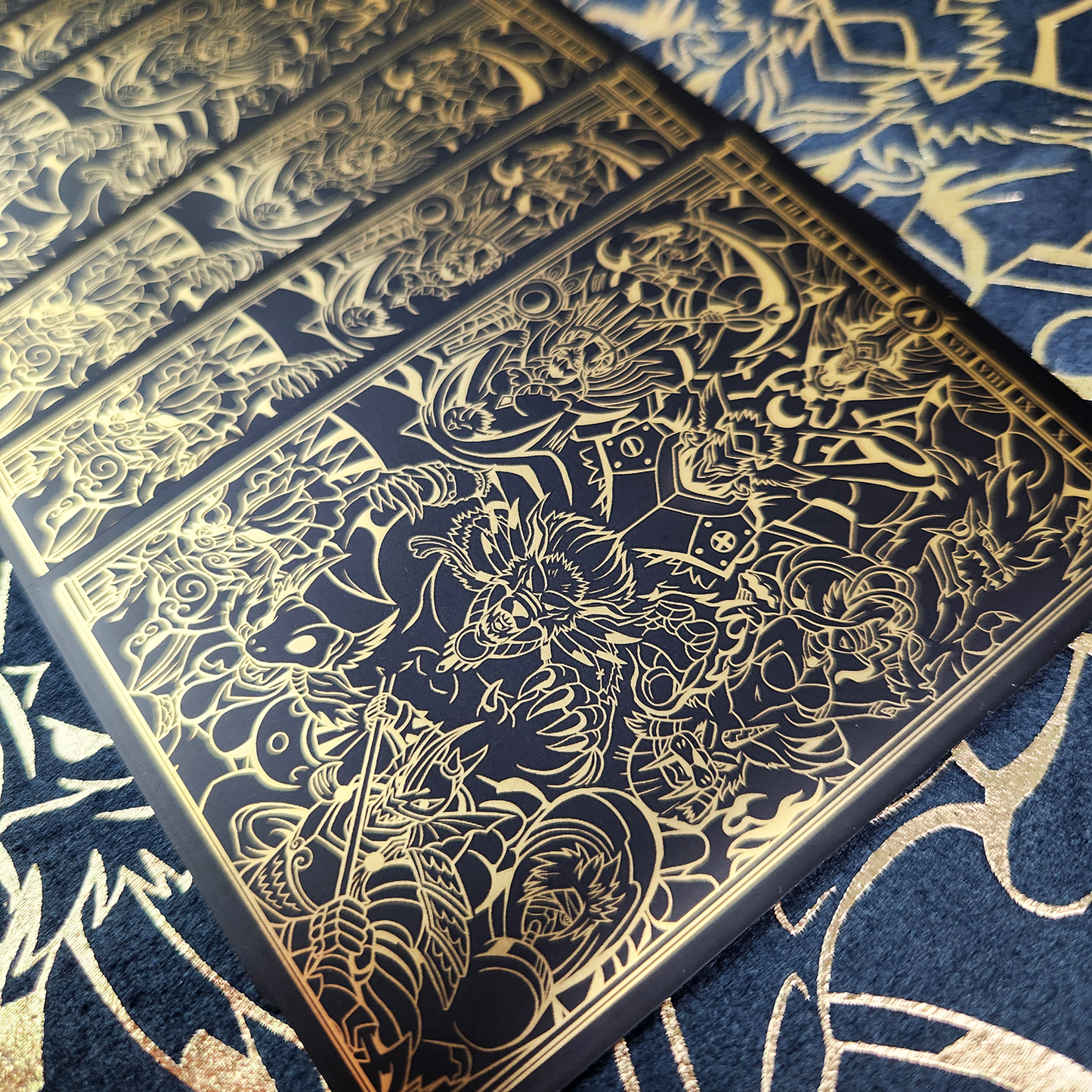 A close-up of a rectangular black card or print featuring intricate gold line art and illustration, laid diagonally over a matching black and gold patterned surface.