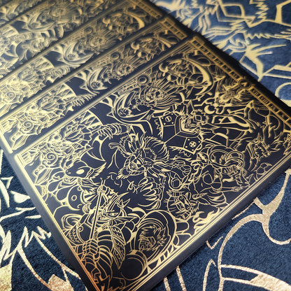 A close-up of a rectangular black card or print featuring intricate gold line art and illustration, laid diagonally over a matching black and gold patterned surface.