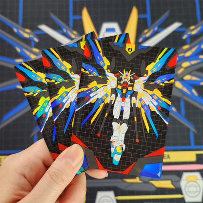 A hand holds three printed cards featuring a colorful mecha illustration on a black grid background, with a blurred blue and gray sci-fi themed backdrop behind.
